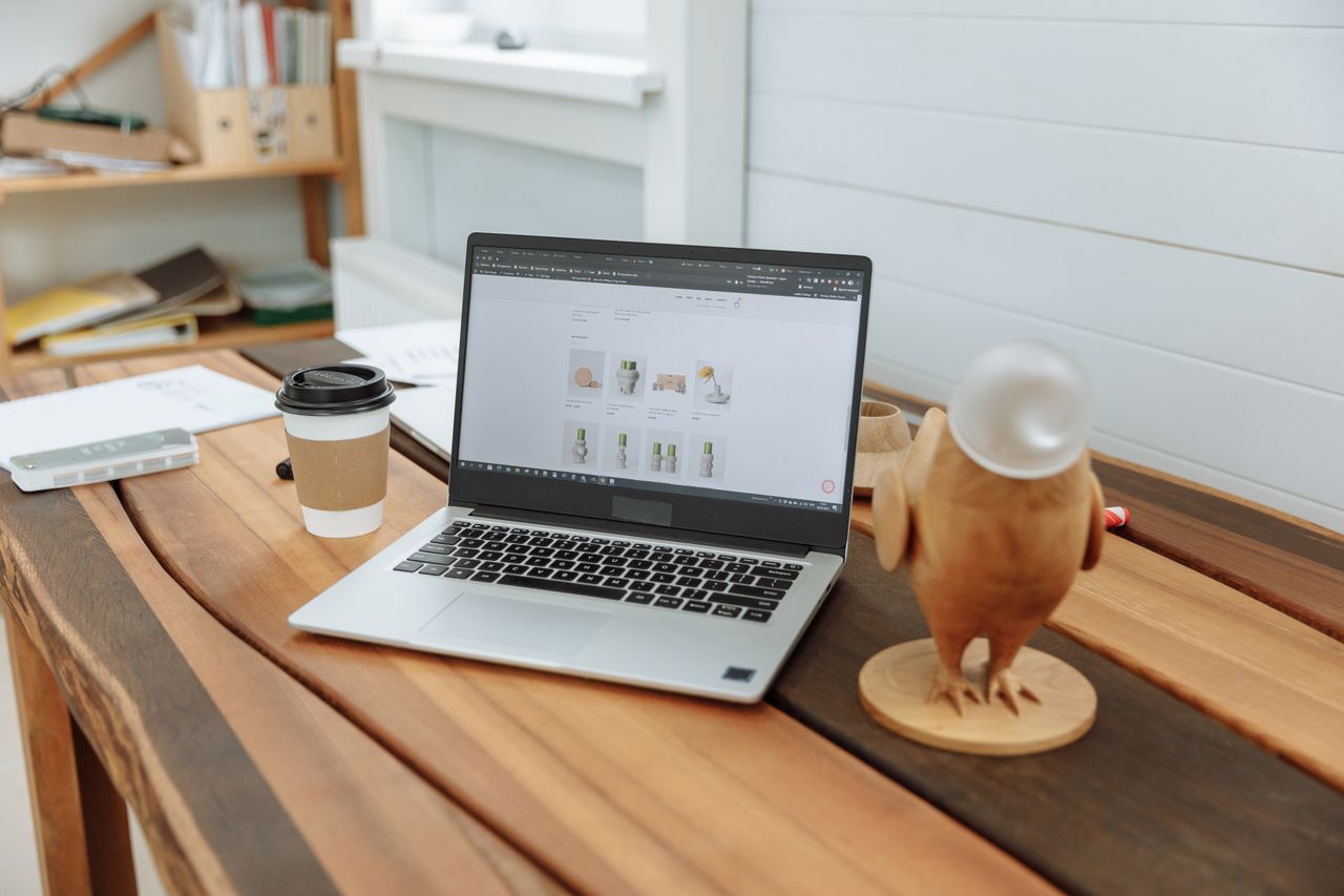 A contemporary office desk setup featuring a laptop, coffee cup, and wooden figurine on a wooden table.