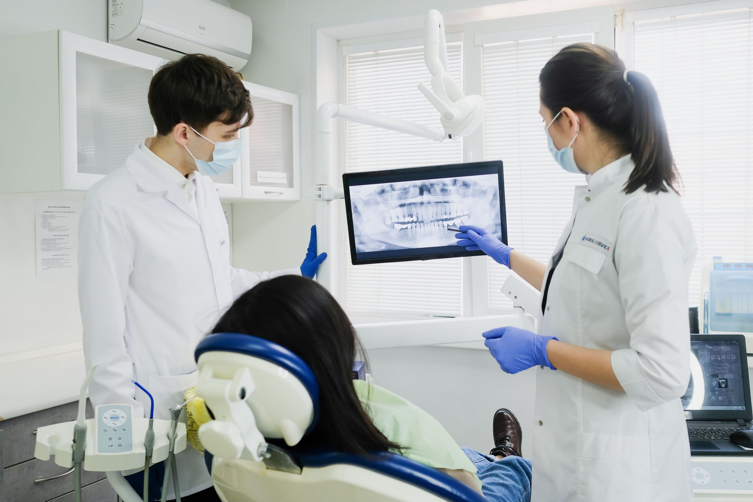 Two dentists examine a dental X-ray with a patient in a modern clinic setting.